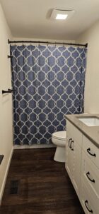 Bathroom with dark wood floor, white vanity with gray countertop, white toilet, and blue patterned shower curtain.