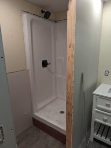 A partially finished bathroom with an installed shower stall, a wooden frame on one side, exposed drywall, and a white vanity with drawers on the right.