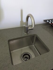 A stainless steel sink with a modern, curved faucet set in a gray countertop. A dish rack is partially visible on the right.