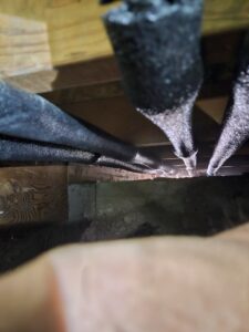 Insulated pipes run beneath a wooden floor, with light shining through gaps in the floorboards above.