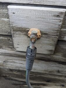 A coaxial cable is loosely connected to an outdoor wall socket with visible corrosion and rust on the connector.