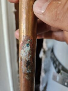 Close-up of a hand holding a copper pipe with visible corrosion and mineral buildup on its surface.
