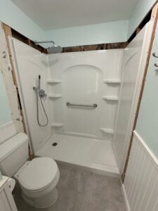 Accessible shower with a handheld showerhead, grab bar, built-in shelves, and partially unfinished walls; toilet visible on the left side.